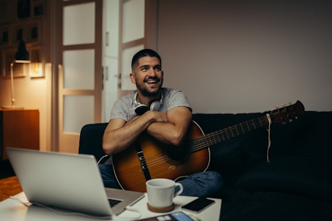 A male musician smiling with his guitar on a couch